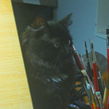 En svart kattunge som tittar på en burk med akvarellpenslar
