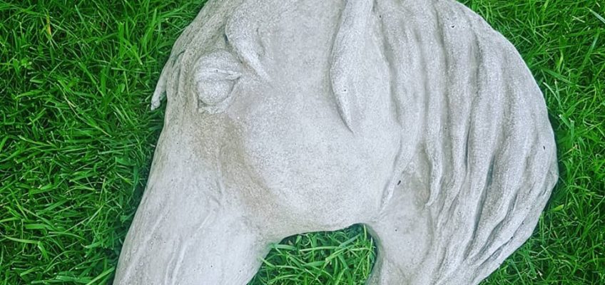 Hästhuvud i betong som ligger på en gräsmatta